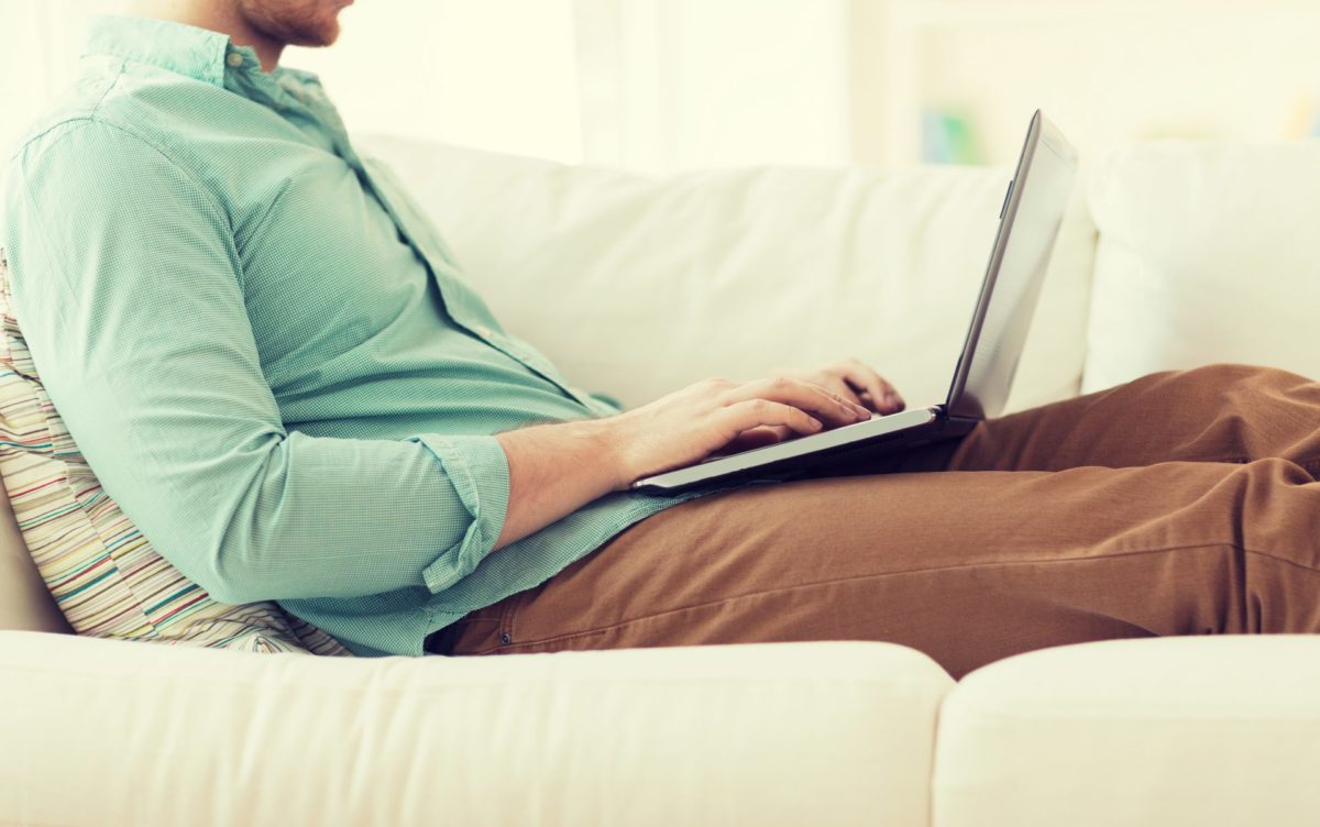 man laying on a sofa typing on a laptop