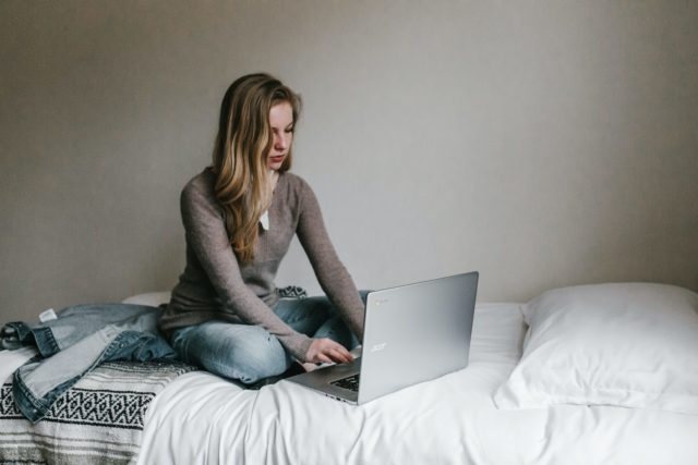 young girl sitting on bed at a laptop
