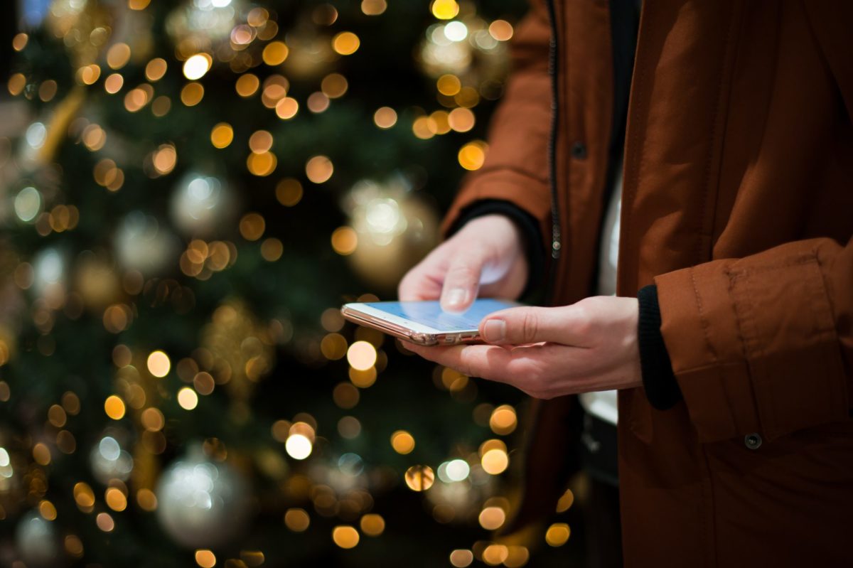 man typing on his phone next to Christmas tree