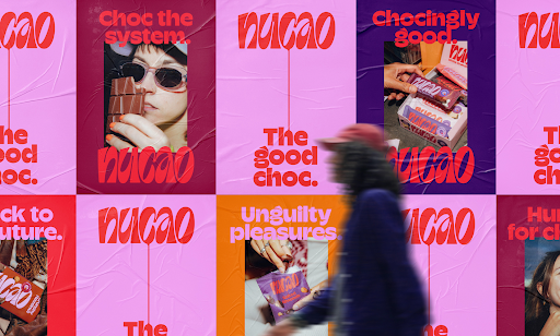 Nu Cao's new branding (bright pink and purple posters with chocolate wrappers and logo) on a wall with a person walking past