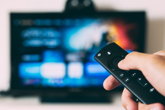 blurred TV (presumably showing adverts) and person holding a remote